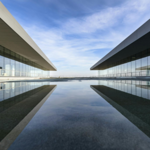 Futuristic glass building mirrored on a still water surface with a cloudy sky.