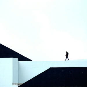 Silhouette of a person walking on a geometric architectural structure under a vast sky.