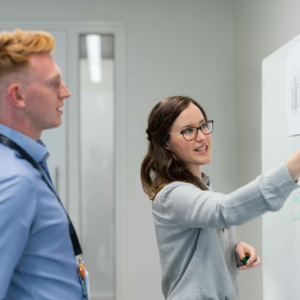 Two colleagues engaged in an office discussion at the whiteboard.